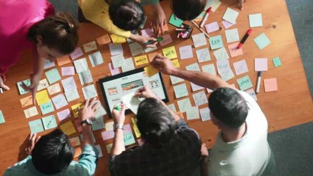 Aerial view of developer team discussing and showing digital program and writing by using Ux Ui design. Top down view of business people develop wireframe prototype for phone and computer. Symposium.