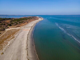 Aerial view of Lido di Volano's pristine shoreline meeting the calm blue waters of the Adriatic Sea. The sandy beach stretches along a tranquil, unspoiled coastal landscape.