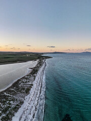 Aerial view of Le Saline beach at Le Tonnare in Stintino, Sardinia, at sunset. The narrow, white sandy beach separates the turquoise-coloured sea from the salt pans.