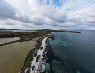 Aerial view of Le Saline beach near Le Tonnare in Stintino, Sardinia. The narrow strip of coast separates the turquoise-coloured sea from the salt pans, overlooked by an old watchtower.