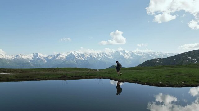 Aerial of hiker with backpack walking by Koruldi lakes in Svaneti mountains. Solo trekker exploring nature, alpine scenery reflecting in water. Adventure travel, outdoor activity, hiking in Georgia.
