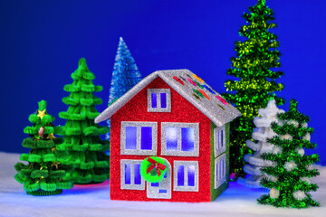On a blue background near a red and green house with blue light in the windows and a decorated roof are multi-colored Christmas trees
