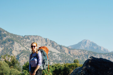 Naklejka premium A young woman with a hiking backpack in the mountains. Trekking in the mountains in summer