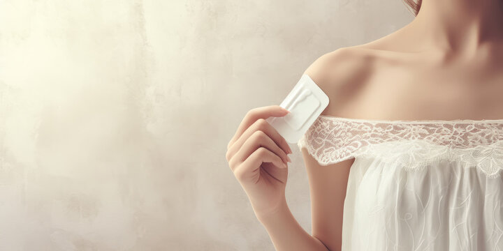 Woman applying birth control patch on shoulder against blank background.