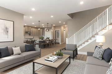 Fototapeta premium Living room and kitchen interior in new home with open concept floor plan. Kitchen features large island, hardwood floors, and stainless steel appliances. Living room is furnished