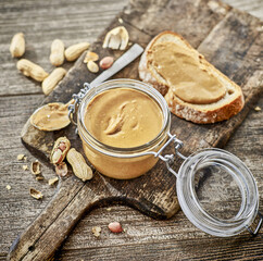 Masło orzechowe w słoiczku i na kromce chleba z orzechami w tle