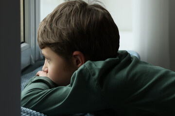 Autism concept. Lonely little boy near window at home