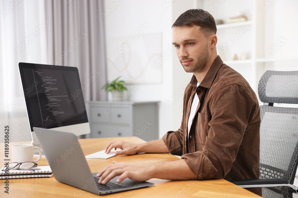 Poster programmer working on laptop and computer at wooden desk indoors
