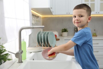 Little helper. Cute boy washing dishes at home