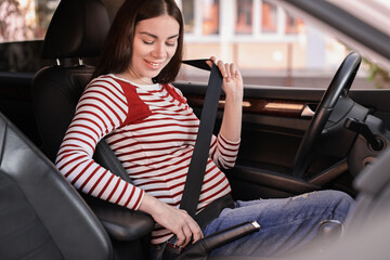 Smiling pregnant woman fastening safety belt in car