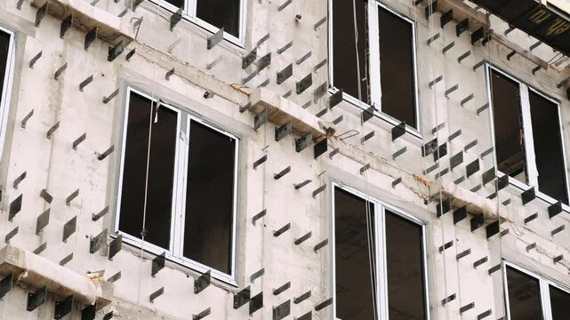 Concrete facade of a multi-storey residential building under construction with windows and metal fasteners for exterior cladding panels. Housing real estate development or office building concept