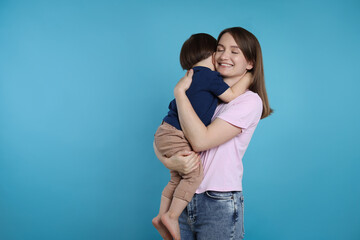 Happy mother with her cute little son on light blue background, space for text