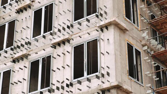 Concrete facade of a multi-storey residential building under construction with windows and metal fasteners for exterior cladding panels. Housing real estate development concept. Close-up shot