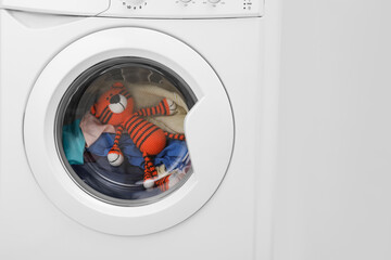 Washing machine with clothes and toy tiger near light wall, closeup