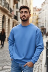 A stylish young man in a blue color sweatshirt mockup stands confidently on a cobblestone street, surrounded by charming buildings. The atmosphere is urban and vibrant, showcasing a modern.