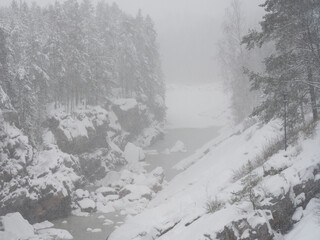 A snowy canyon with snow-covered rocks and trees in a winter forest. A soft mist envelops the landscape, creating an atmosphere of northern winter nature