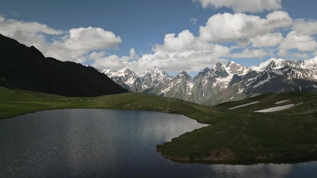 Aerial view of Koruldi mountain lakes and Svaneti peaks. Man hiker walks by. Snow patches and green meadows. Scenic natural beauty. Summer trekking, outdoor adventure Drone shot