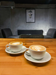 Obraz premium Two steaming lattes with intricate latte art sit on a wooden table in a cozy Istanbul cafe, perfectly capturing a calm spring afternoon indoors