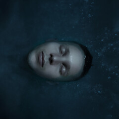 Fototapeta premium Serene portrait of a young man floating in dark water with eyes closed, evoking calm and introspection. Dreamy and moody atmosphere, perfect for themes of mindfulness, relaxation, and solitude.