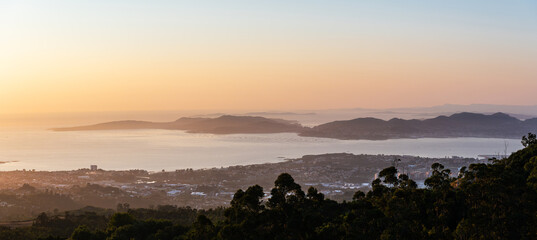 Aerial view of a vibrant orange sunset over the Ría de Vigo estuary in Galicia, Spain, with the serene Ons Islands silhouetted in the background. © Andrés García