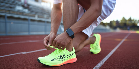 Athlete Tying Running Shoes on Track Before Training.  Close-up of a runner tying neon green and orange running shoes on a red track, preparing for a workout.