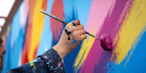 Young Artist Creating Vibrant Street Mural. Close-up of an artist's hand applying a stroke of bright magenta paint to a colorful, abstract mural.