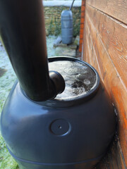 Closeup of an iced over, full rainwater butt with downpipe, standing outside during winter, next to...