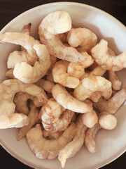Closeup overhead shot of frozen raw king prawns, defrosting in a bowl.