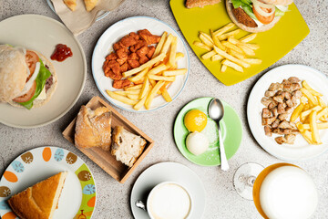 Table full of plates with delicious food like burgers, french fries, meat, bread, coffee and beer, ideal for restaurant menu