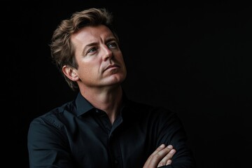 Fototapeta premium Man looking up with arms crossed wearing a black shirt against a dark background