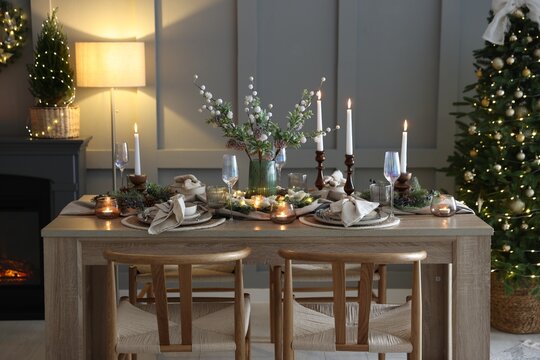 Christmas table setting with stylish dishware, glasses and burning candles in festive decorated room