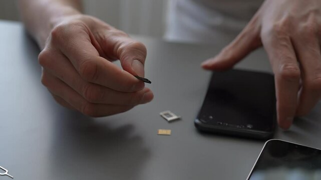 Close-up cropped shot of technician skillfully replacing sim card in smartphone sitting on grey table with the sim card and tray clearly visible for detailed observation. Shooting in slow motion.