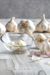 Fresh organic garlic bulbs and bowl of peeled cloves on wooden background. Selective focus