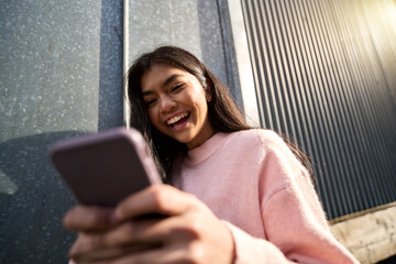 Happy cheerful Asian teen girl blogger using mobile phone standing on street. Smiling female model...