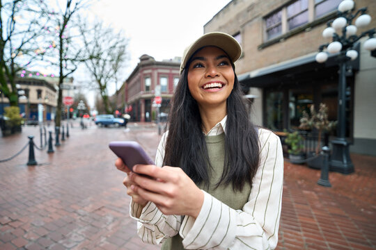 Smiling cool teen girl holding mobile cell phone having fun outdoors with cellphone in hands. Happy cheerful Asian teenager using smartphone chatting online or doing ecommerce shopping in the city.