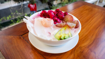 A bowl of colorful fruit dessert, including dragon fruit, grapes, avocado, and coconut slices, served with milk