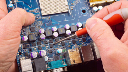 In the photo, the hands of an old master perform repair and maintenance of electronic components of a computer. Close-up.