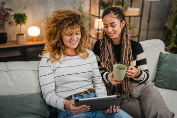 cheerful female friends sit on sofa and enjoy while use digital tablet