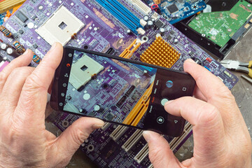 An electronics repair technician uses a smartphone to scan computer boards.