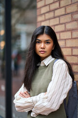 Vertical portrait of confident Asian teenage female college student standing in the city. Unsmiling smart cool teen school girl looking at camera outdoors posing with backpack in campus area.