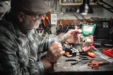 An elderly electronics repairman works in a home workshop.