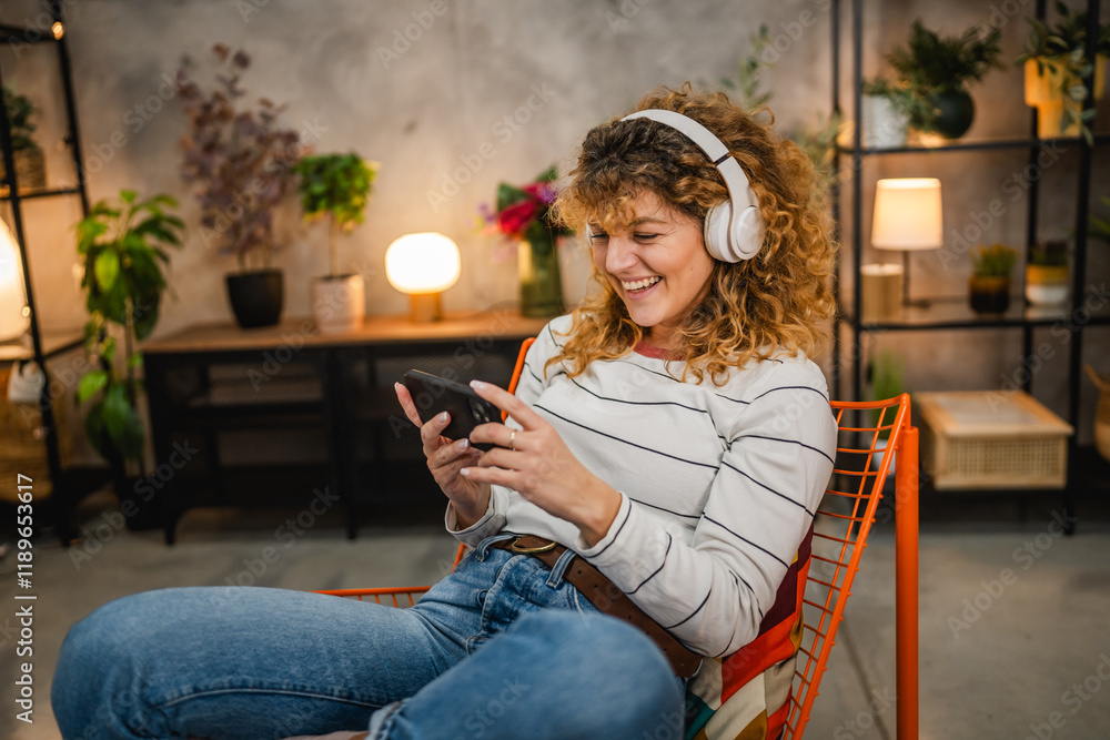 Wall mural happy adult woman with headphones play video games on mobile phone