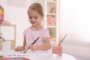 Smiling girl drawing at white table in kindergarten. Space for text