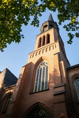 Fototapeta premium Historic Brick Church Tower with Sunlight and Green Foliage : Generative AI