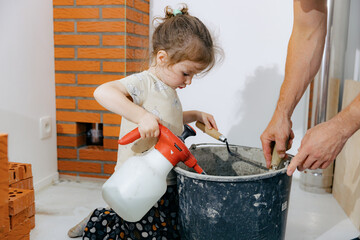 A girl wets cement in a bucket with water from a spray bottle.