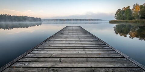 Naklejka premium Serene wooden pier extending into calm lake at dawn surrounded by fog and lush trees