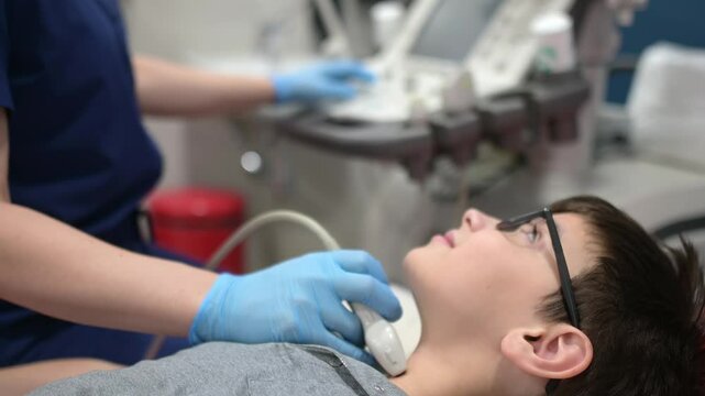 Doctor making sonogram of thyroid gland for boy using scanner machine. Female doc runs ultrasound sensor over patient neck for scanning of thyroid gland and lymph nodes. Checkup of internal organs