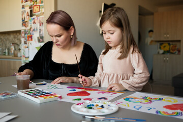 Fototapeta premium A mother and her young daughter engage in creative art activities, painting colorful designs and bonding in a cozy home setting. The moment portrays love, creativity, and family collaboration.