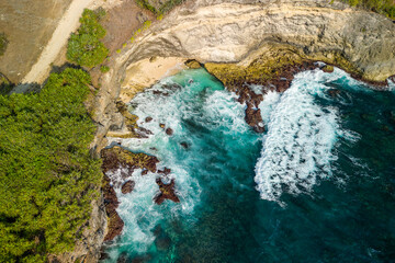 Birds-eye view of tropical ocean waves crashing against a small beach and rocks
