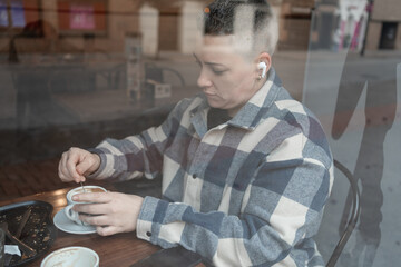 Woman wearing earbuds is stirring coffee in cafe